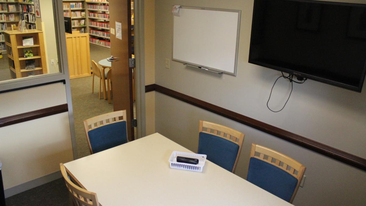 Study room B, with table and chairs, wall-mounted television, and dry-erase whiteboard